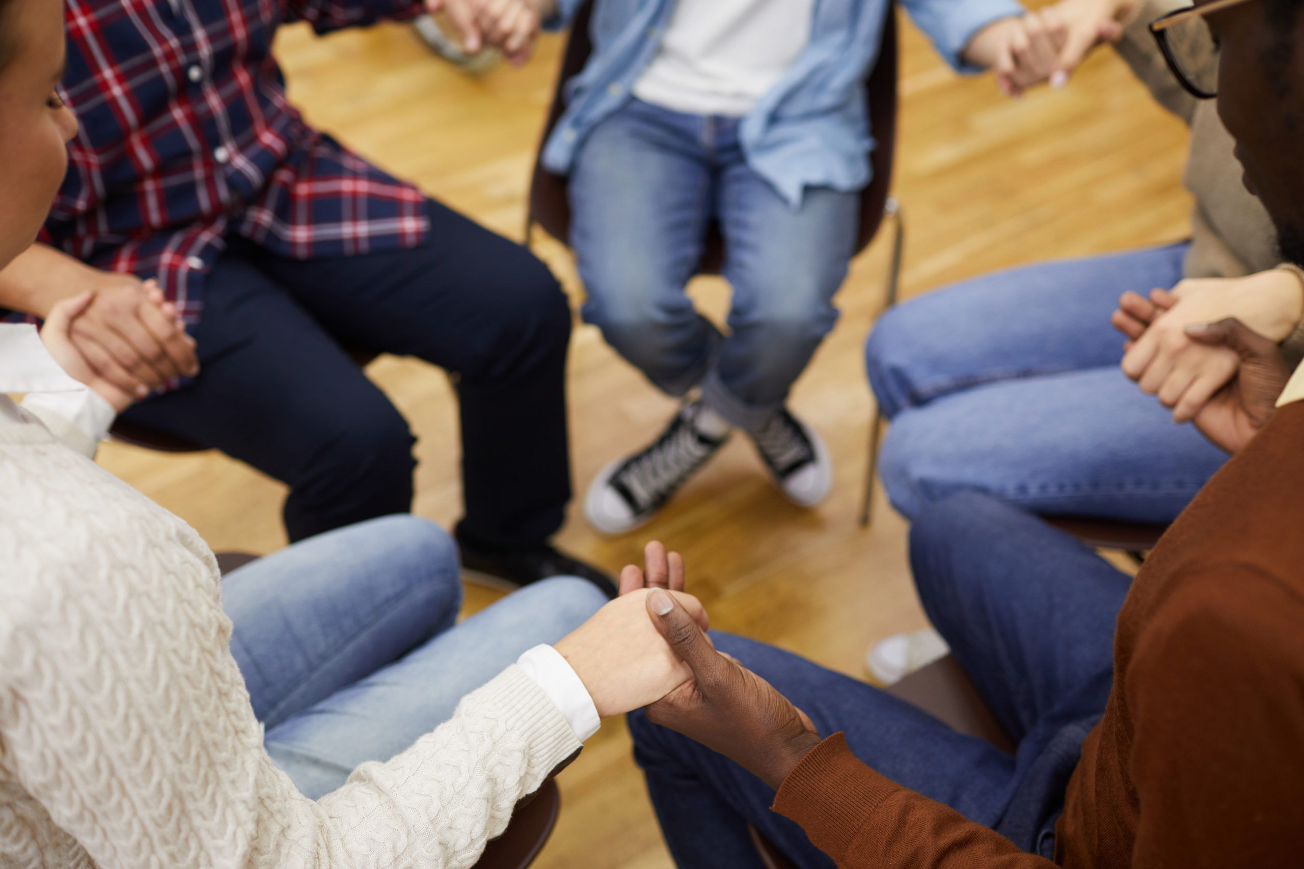 High angle closeup of unrecognizable people sitting ion circle and holding hands during support group meeting, cpy space