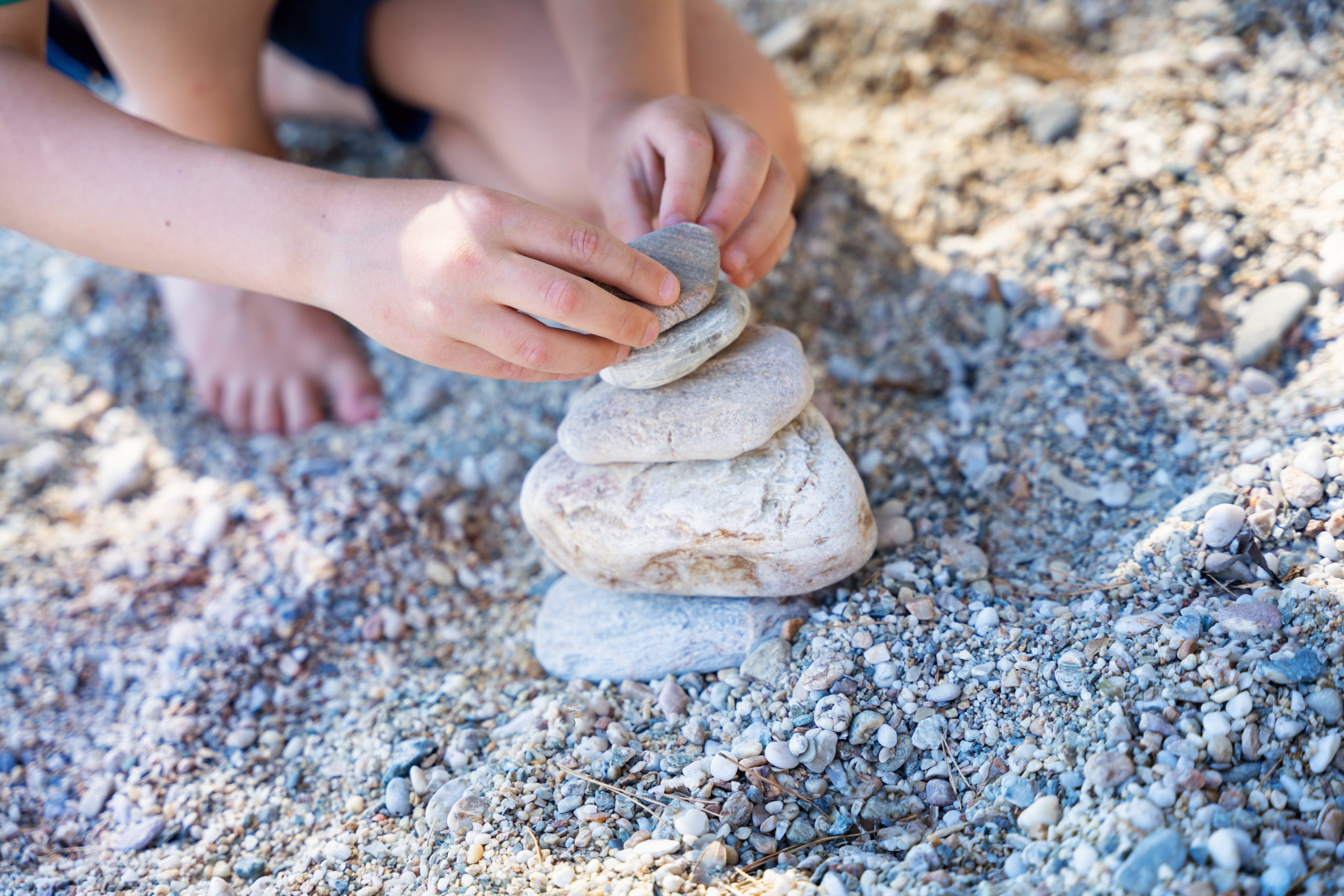 Child building a pile of stones on beach.Playing and  relaxation at sea. Stone cairn on natural background. Concept balance.